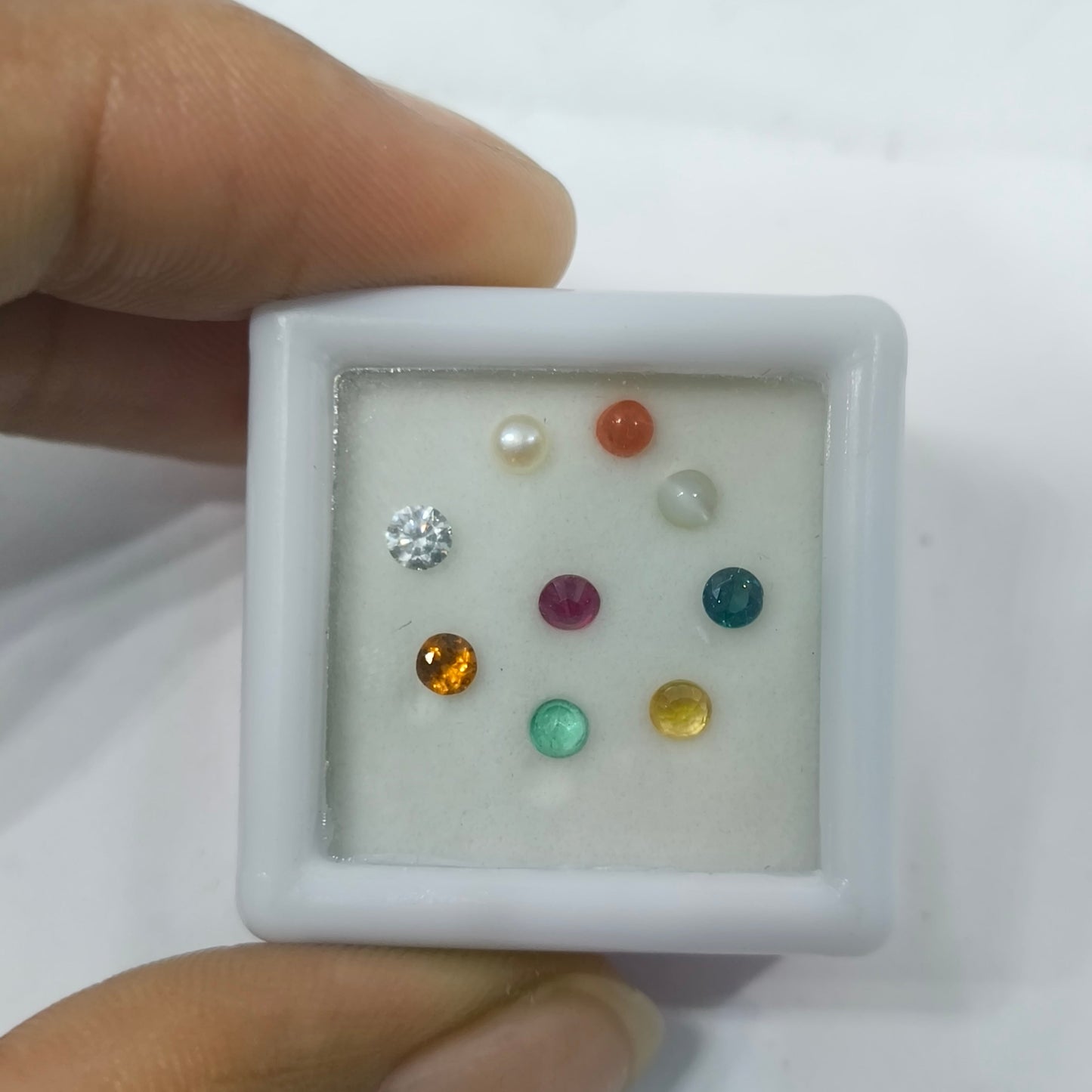 Small white box with various gemstones held by a hand against a white background